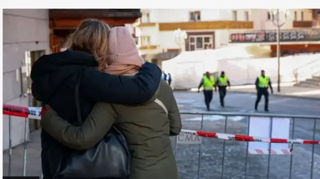 Aworan obinrin meji ti wọn di mọra wọn nipo ibanikẹdun, pẹlu awọn ẹṣọ alaabo mẹta to n rin bọ