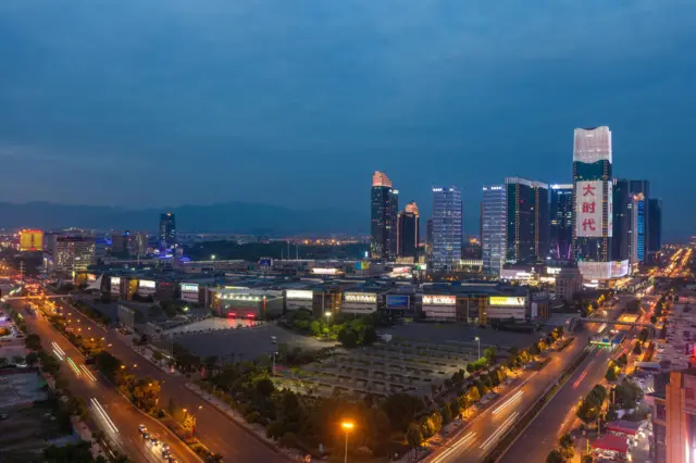 Foto panorâmica de cidade Yiwu à noite, de onde se pode ver prédios iluminados e avenidas