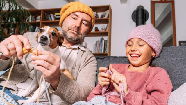 Pai e filha tricotando, com um cachorrinho no colo.