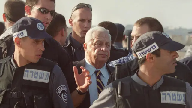 O então primeiro-ministrobet esportesIsrael Ariel Sharon cercado por policiais ao deixar a mesquitabet esportesal-Aqsa,bet esportes2000