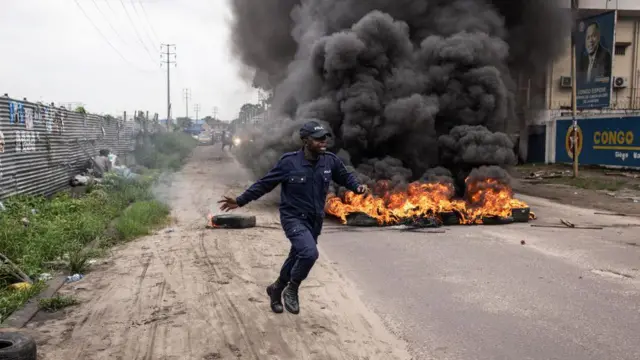 Umupolisi ari kwirukana abaje mu myigaragambyi ari iruhande rw'amapine ari gushya