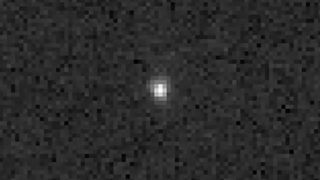A cluster of white pixels form a white dot in the middle of the image against a highly pixelated black and grey background.