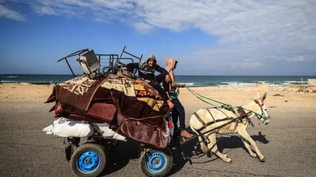 Warga Palestina yang melarikan diri dari Khan Younis di jalan pantai menuju Rafah lebih jauh ke selatan menaiki kereta keledai membawa barang-barang mereka pada 25 Januari 2024, di tengah pertempuran yang terus berlanjut antara Israel dan kelompok militan Palestina Hamas