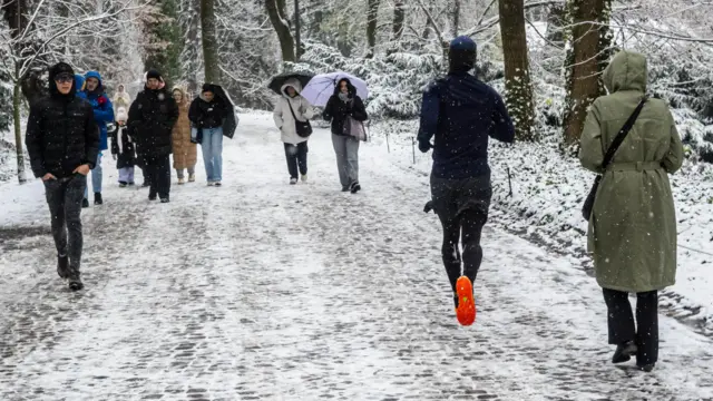Osoby spacerują, a jedna biegnie po zaśnieżonej alejce w parku