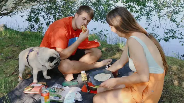 Una mujer y un hombre noruegos están sentados charlando de sobremesa en un comedor donde está servido un banquete de tacos. Beben cerveza y tienen velas encendidas.