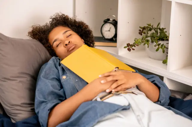 Adolescente tirando uma soneca abraçada com livro