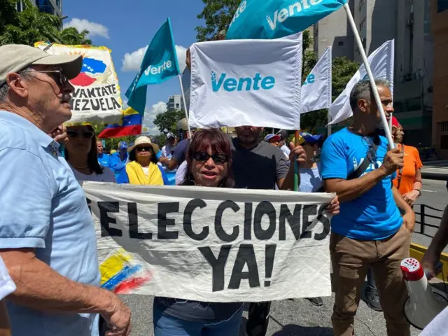 En medio de una multitud, una mujer muestra una pancarta que dice "Elecciones ya".