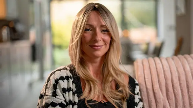 艾伦留着一头长金发，坐在沙发上，对着镜头微笑。