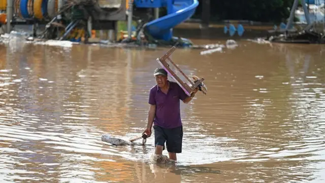 荷物を手にした半そでシャツ、短パン姿の人が水浸しになった場所を膝までつかりながら歩いている