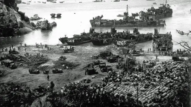 মার্কিন যুদ্ধজাহাজ ও যানগুলো তীরে নোঙর করা আছে। প্রতিটি জাহাজের সামনে তিন বা চারটি সংখ্যা লেখা দেখা  যাচ্ছে। গভীরে সমুদ্রে আরো জাহাজ রয়েছে। সৈকতে সৈন্য ও যানবাহন রয়েছে এবং উপকূলরেখার কাছাকাছি রসদপত্র স্তূপ করে রাখা হয়েছে।