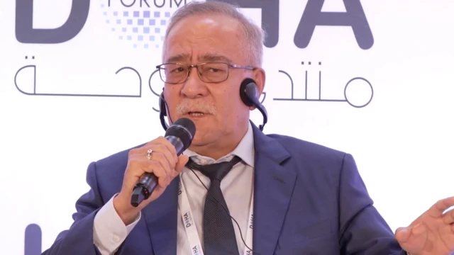 نماینده ازبیکستان برای افغانستان با دریشی آبی، نیکتایی سیاه که گوشی در گوش و مایک در دست دارد و در حال سخنرانی است.