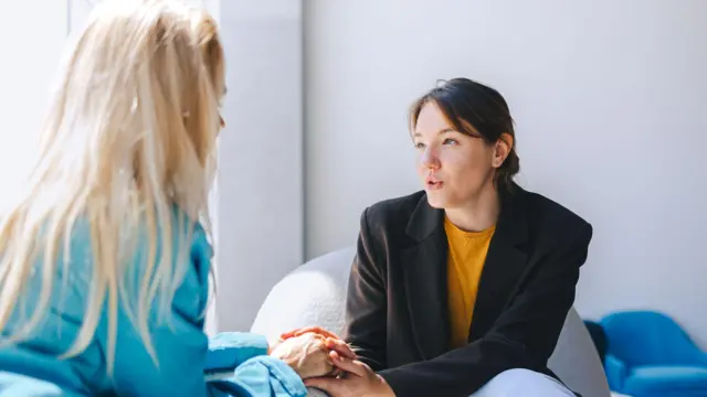 Duas mulheres sentadas uma de frente para a outra conversam. 