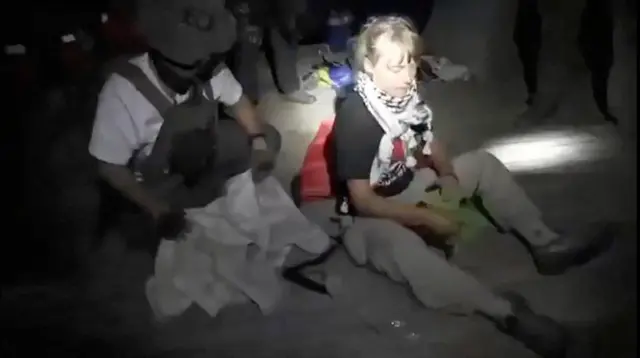 Greta sentada no escuro, ao lado de soldado; ela olha para baixo
