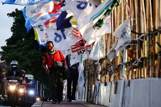 Orang-orang berjalan di samping bendera yang mewakili berbagai partai politik yang dipasang di sepanjang jalan-jalan di Jakarta, Indonesia pada 23 Januari 2024.