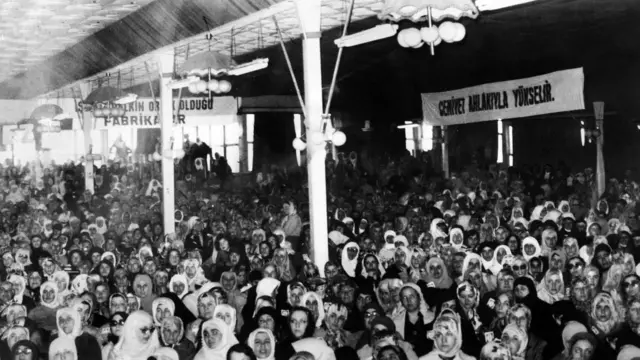 Şenler'i bir konferansta dinlemeye gelen kadınlar. Hemen hemen hepsi başörtülü. Sağda yukarıdaki pankartta "Cemiyet ahlakıyla yükselir" yazıyor.