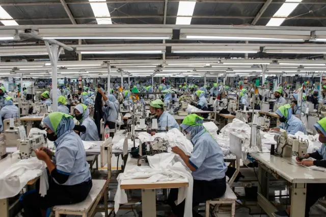 Para pekerja sedang berada di dalam pabrik dan tekun dengan mesin jahitnya.