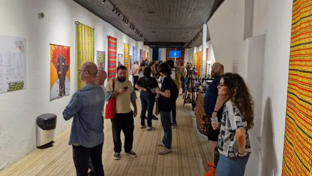 Kilka osób ogląda dzieła sztuki wyeksponowane po obu stronach białych ścian galerii.