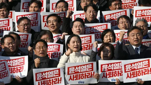 Anggota parlemen membawa plakat bertuliskan "Yoon Suk Yeol harus mengundurkan diri" pada 4 Desember