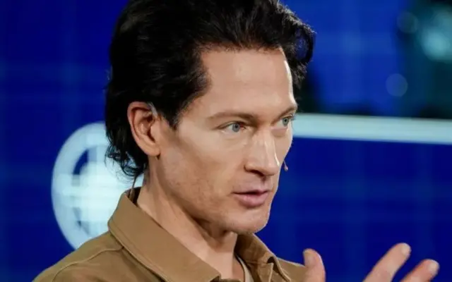 ব্রায়ান জনসন কথা বলার সময় হাত তুলে কিছু একটা বোঝানোর চেষ্টা করছেন
