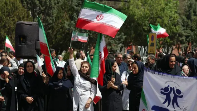 Медицинские работники, держащие иранские флаги, принимают участие в акции протеста против американо-израильских ударов по медицинским учреждениям у больницы имени имама Хомейни в Тегеране, Иран, 6 апреля 2026 года.