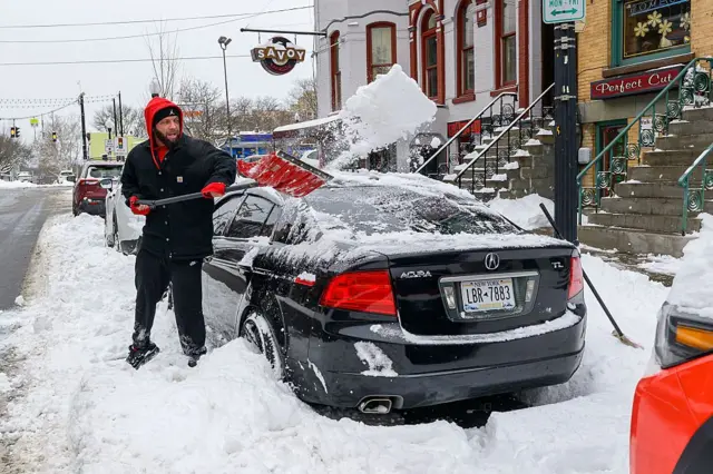 Un hombre quita la nieve alrededor de un auto en Albany
