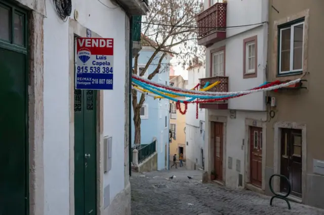 Uma placa de "Vende" em frente a um prédio residencial no bairro de Alfama, em Lisboa, Portugal.