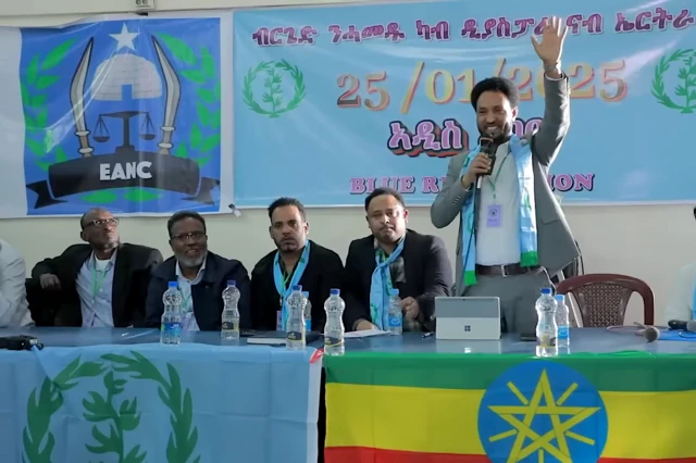 የኤርትራ ተቃዋሚዎች በአዲስ አበባ ባዘጋጁት ኮንፈረንስ ላይ አመራሮች መድረክ ላይ ቁጭ ብለው። የድምጽ ማጉያ የያዘው የብርጌድ ንሓመዱ አመራር አቶ በየነ ቆሞ እጁን እያውለበለበ፤ የብርጌድ ንሓመዱ አርማ እና የኢትዮጵያ ባንዲራ ጎን ለጎን ይታያል