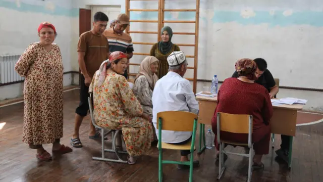 Ayollr va erkaklar maktab partasi atrifida o'tirib, hujjat rasmiylashtirmoqdalar