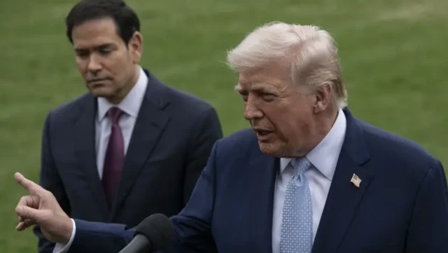 دونالد ترامپ در فضای باز درحالی که با انگشتش به سمت جایی اشاره می‌کند، پشت میکروفون در حال صحبت است، وزیر خارجه آمریکا پشت سر او ایستاده است