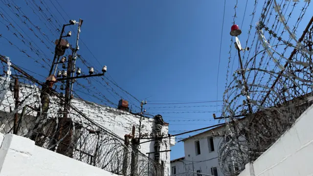 Голубое небо над белыми стенами, обтянутыми колючей проволокой и бритвенной проволокой.