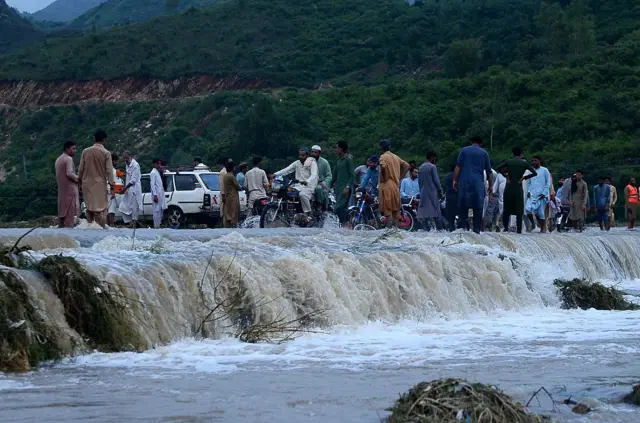 বন্যার পানির স্রোতের মধ্যেই ভেঙে যাওয়া রাস্তা দিয়ে চলাচল করছে মানুষজন ও যানবাহন