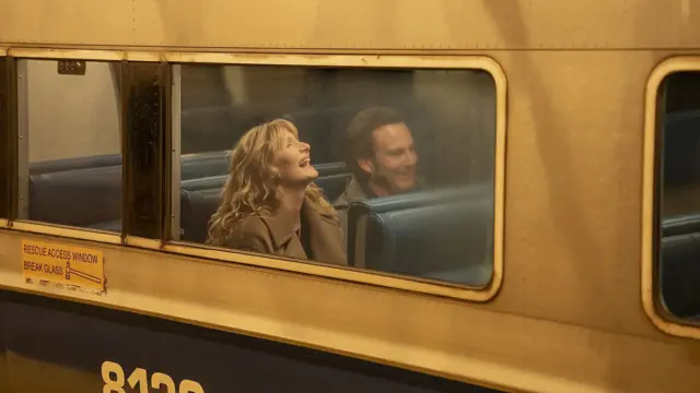 У вікні жовтого автобуса видно чоловіка та жінку, які сміються