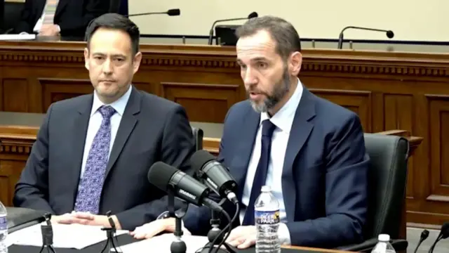 マイクの立つ机に向かい、書類を手元に置き、前を見て発言するスミス氏