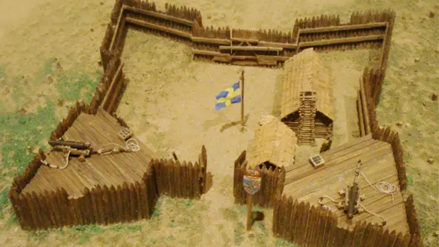 Maqueta de Fuerte Cristina, el primer asentamiento permanente europeo en el valle del Delaware, con empalizadas de madera, edificios de troncos y la bandera sueca en el centro del recinto.
