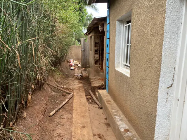 Urebeye inyuma y'inzu, ubona aho babomoye urukuta kugira ngo bakure imirambo mu cyobo bivugwa ko yari yaracukuye agashyiramo abo yishe