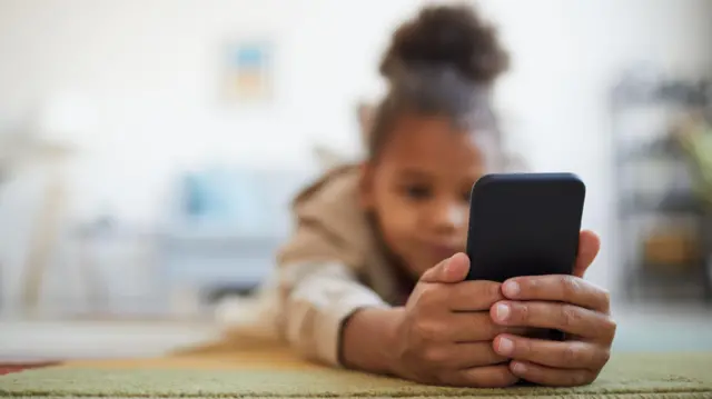 Close de uma menina segurando um smartphone enquanto está deitada no chão 
