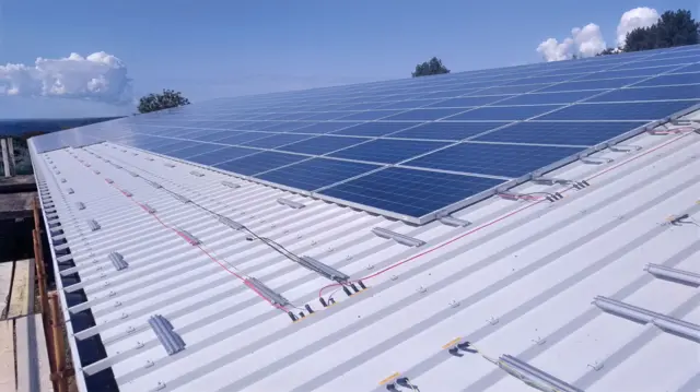 Un techo, parcialmente cubierto de paneles solares, contra un cielo azul de fondo.