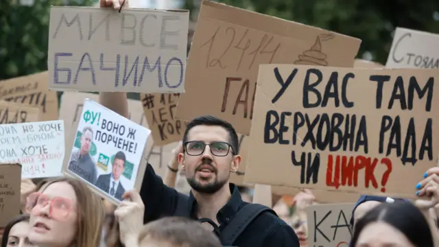 Молодые люди с картонными и бумажными плакатами, на одном из плакатов изображены Зеленский и Ермак.