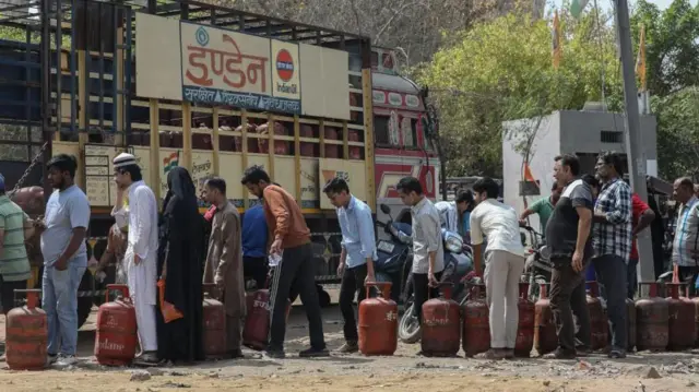 赤茶色のボンベを足元に置いた人が屋外に行列している。