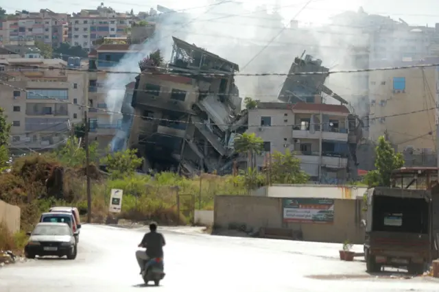 Un hombre en moto circula cerca de un edificio bombardeado por Israel.