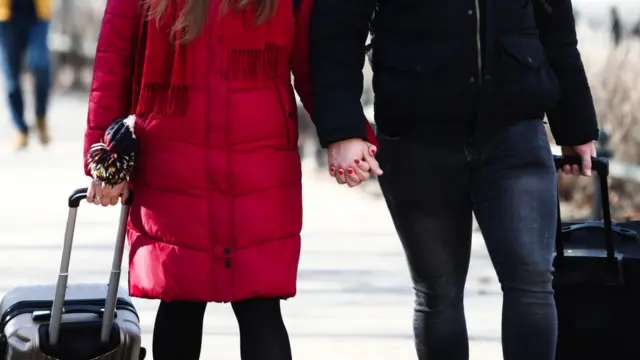 Pasangan bergandengan tangan di pinggir jalan.