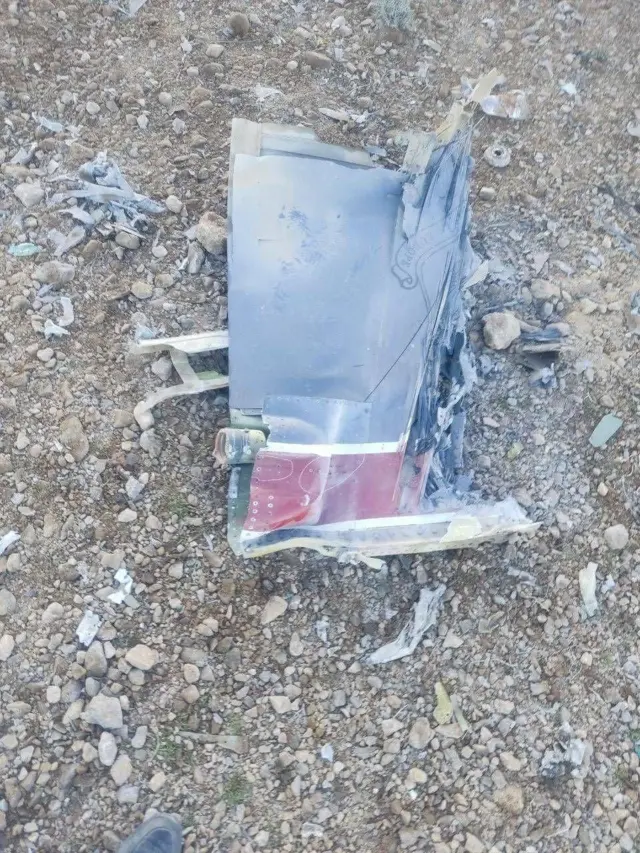 砂利の上に飛行機の一部と思われる破片が落ちている。灰色で先端に赤と白の縞が入っている