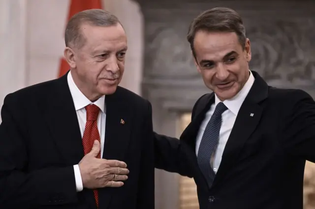 Cumhurbaşkanı Erdoğan ve Yunanistan Başbakanı Miçotakis yan yana gülümsüyorlar.