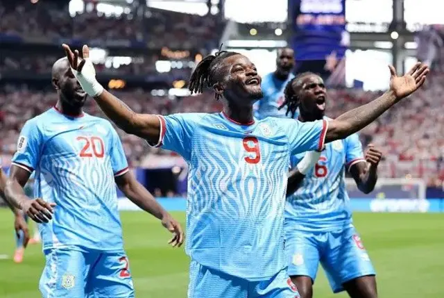 Brian Cipenga wear DR Congo national jersey, e dey in di middle of im two teammates.