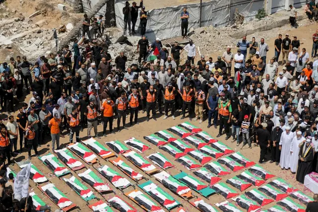 Los dolientes se colocan cerca de cuerpos envueltos en banderas palestinas durante un funeral masivo en la ciudad de Gaza, Franja de Gaza, el 4 de agosto de 2026. Los restos de 112 miembros de las familias Abu Sharia y Al-Hasayneh fueron recuperados de los escombros de su hogar tras un ataque israelí