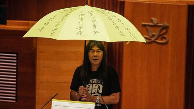 Leung "Long Hair" Kwok-hung, a lawmaker and chairman of the League of Social Democrats, holds a yellow umbrella while standing next to a prop representing the Hong Kong electoral reform proposal known as "831" during an oath-taking ceremony in the chamber of the Legislative Council in Hong Kong, China, on Wednesday, Oct. 12, 2016