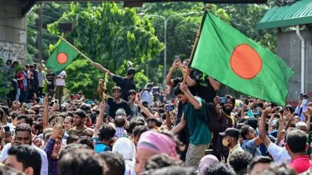 ढाकामा बाङ्ग्लादेशको झण्डा बोकेर उभिएका मानिसहरू
