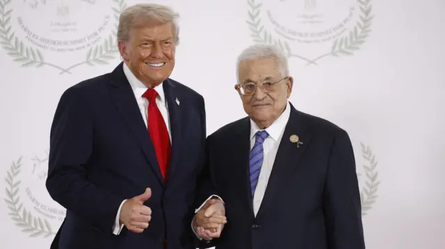 El presidente Trump, sonriente y con un pulgar alzado, junto al presidente de la Autoridad Palestina, Mahmud Abás, al que agarra de la mano. 