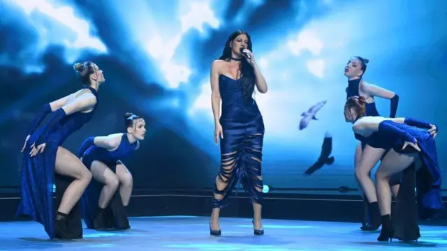 Ана Машуловић окружене плесачима, носи тамно плаву хаљину, има дугу црну косу