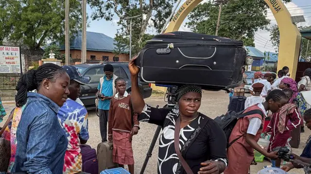 Des proches et des élèves portent des bagages – une femme au centre de la photo a une grosse valise sur la tête – en sortant d'un établissement d'enseignement secondaire situé à la périphérie d'Abuja, la capitale, après la fermeture ordonnée par le gouvernement de 47 internats à travers le pays.